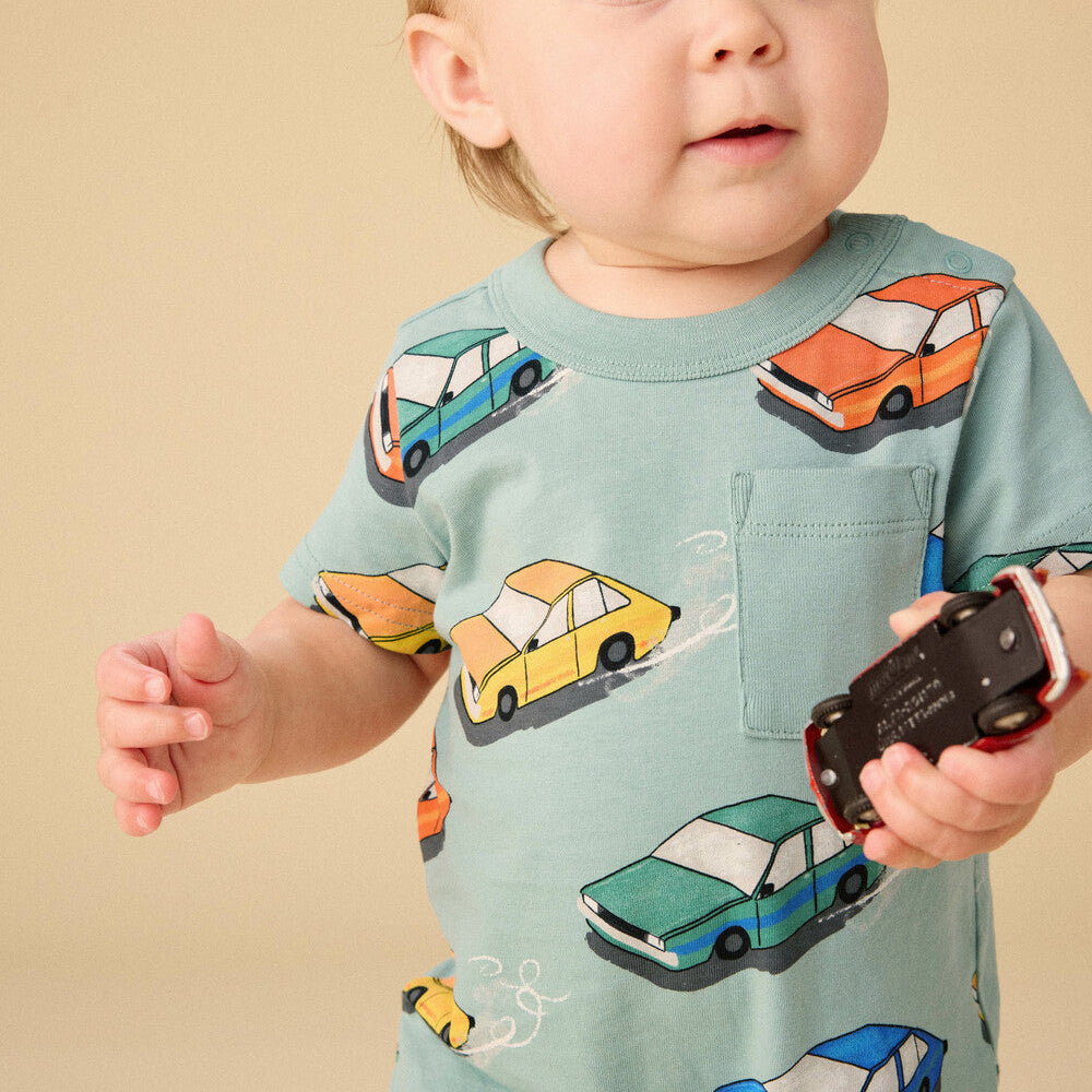 Baby wearing a shirt with car prints holding a toy car against a beige background