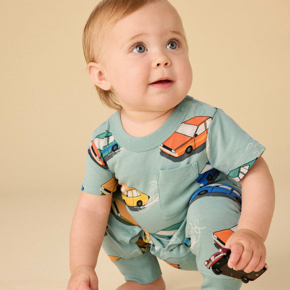 Baby wearing a green outfit with vehicle prints on a beige background