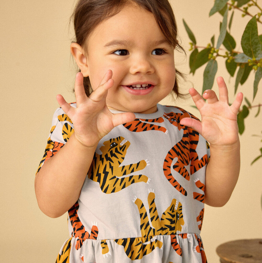 Child wearing a dress with tiger pattern against a beige background