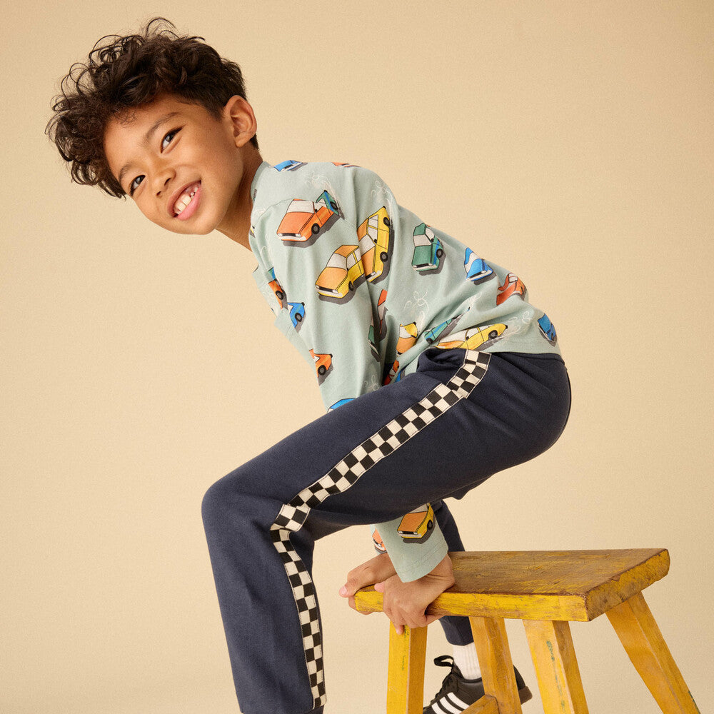Child sitting on a wooden stool wearing a colorful shirt and navy pants with checkered stripes.
