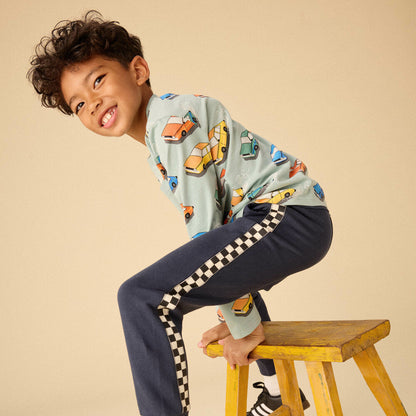 Child sitting on a wooden stool wearing a colorful shirt and navy pants with checkered stripes.